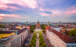 Blick auf eine Stadt mit Turm und umgebenden Gebäuden bei Sonnenuntergang.