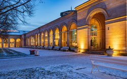 Beleuchtetes historisches Gebäude mit großen Rundbogenfenstern bei Dämmerung und Schnee.