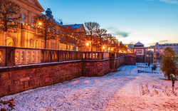 Historisches Gebäude bei Sonnenuntergang im Winter mit beleuchteten Bäumen und Schnee.