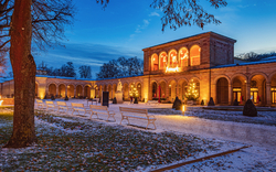 Bad Kissingen im Winter mit Schnee bedecktem Boden, beleuchtetes Badehaus und Bäume im Hintergrund.