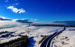 Schneebedeckte Landschaft mit gewundener Straße und blauem Himmel.