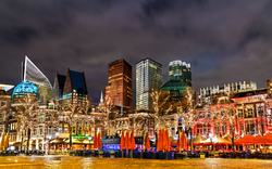 Beleuchtete moderne Stadtgebäude bei Nacht mit Lichtern und Wolken am Himmel.