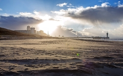 Strand mit Blick auf Pier und Gebäude im Sonnenuntergang.