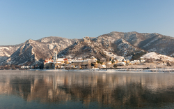 Fluss mit Spiegelung eines Dorfes und schneebedeckten Bergen im Hintergrund.