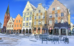 Bunte historische Gebäude mit schneebedecktem Platz und Kirche im Hintergrund.