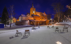 Verschneiter Platz nachts mit beleuchteter Kirche im Hintergrund.