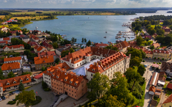 Luftaufnahme einer Stadt mit rotem Dächern an einem Seeufer, Boote am Pier.