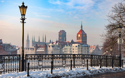 Verschneite Stadtansicht mit alten Gebäuden und Laternen im Vordergrund.
