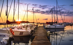 Yachthafen bei Sonnenuntergang mit Segelbooten am Steg.