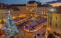 Weihnachtsmarkt mit geschmücktem Baum und hellen Lichtern in einer Stadt bei Abenddämmerung.