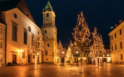 Beleuchteter Platz mit Kirche und geschmückten Bäumen in der Nacht.