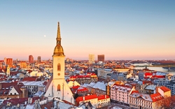 Skyline von Bratislava bei Sonnenuntergang im Winter, mit einer Kirche im Vordergrund.