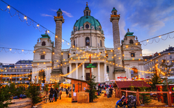 Barocke Kirche bei Sonnenuntergang, umgeben von beleuchtetem Weihnachtsmarkt und Menschen.