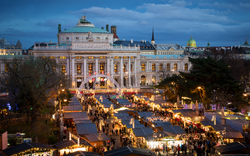 Weihnachtsmarkt vor einem beleuchteten historischen Gebäude am Abend.