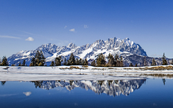 Verschneite Berge spiegeln sich in einem stillen See unter blauem Himmel.