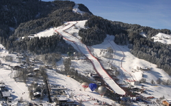 Skipiste mit Zielbereich in verschneiter Berglandschaft und Heißluftballons.