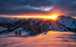 Sonnenuntergang hinter verschneiten Bergen und bewaldeten Hügeln.