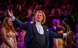 Ein Dirigent in festlicher Kleidung dirigiert ein Orchester auf einer Bühne.