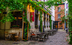 Idyllische, mit Pflanzen bewachsene Gasse mit Außenrestaurierungstischen.