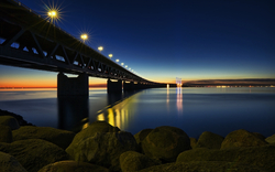 Beleuchtete Brücke bei Sonnenuntergang über ruhigem Wasser.