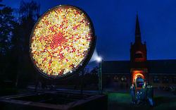 Leuchtende Kunstinstallation im Freien bei Nacht vor einem beleuchteten Gebäude.