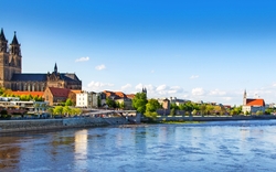 Ansicht des Magdeburger Doms mit Elbe im Vordergrund bei klarem Himmel.