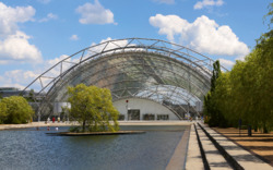 Moderne Glashalle mit Wasserbecken und Himmel im Hintergrund.