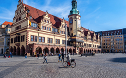Historisches Gebäude mit Turm auf großem, belebtem Platz bei blauem Himmel.