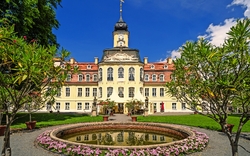 Historisches Gebäude mit rundem Brunnen und Blumen im Vordergrund.