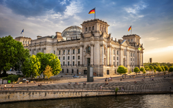 Reichstagsgebäude in Berlin bei Sonnenuntergang mit deutschen Flaggen.