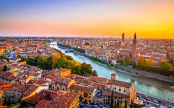 Stadtansicht von Verona bei Sonnenuntergang mit Fluss und historischen Gebäuden.