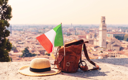 Hut, Rucksack und italienische Flagge vor Stadtpanorama.