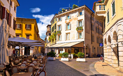 Sonniger Stadtplatz mit Café und historischen Gebäuden.