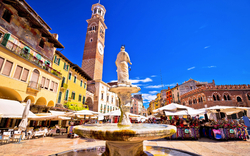 Marktplatz mit Brunnen und Uhrturm an einem sonnigen Tag in einer europäischen Stadt.