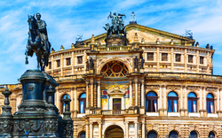 Barockes Opernhaus mit Reiterdenkmal im Vordergrund und blauem Himmel im Hintergrund.