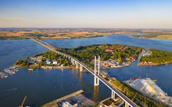 Luftaufnahme einer Brücke über einem Fluss mit Insel und Landschaft im Hintergrund.