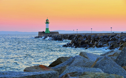 Leuchtturm bei Sonnenuntergang an einer felsigen Küste mit blauem Meer.