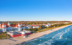 Küstenlandschaft mit historischen Gebäuden am Strand und welligem Meer bei blauem Himmel.
