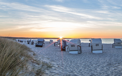 Strandkörbe am Sandstrand bei Sonnenuntergang.