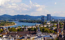 Stadtansicht mit Kirchen, Fluss und Bergen im Hintergrund.