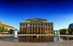 Ein Opernhaus vor einem Brunnen unter blauem Himmel.