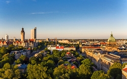 Stadtansicht von Leipzig mit markanten Gebäuden und grünem Vordergrund bei klarem Himmel.