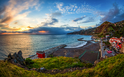 Küstenlandschaft mit Meer, Strand und bunten Häusern bei Sonnenuntergang.