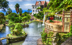 Ein tropischer Garten mit Teich, Palmen, Wasserspielen und historischem Gebäude im Hintergrund.